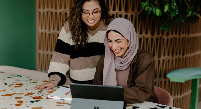 Two young women smiling in front of a laptop.