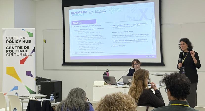 A photograph of the workshop where Miriam Kramer, Executive Director of Government Relations & Public Policy at OCAD University, introduces the program of the day to participants, with the Cultural Policy Hub banner visible and the Hub’s Policy Advisor Clara Godbillon-Vasseur in the background
